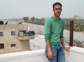 Bilal Jadou inside the Aida refugee camp, overlooking the separation wall and his home on the other side (Nora Barrows-Friedman)