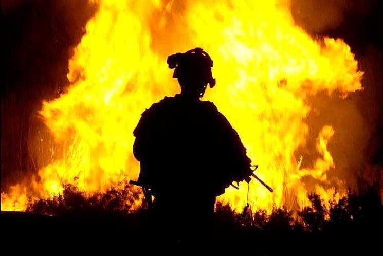 U.S. soldier looks on as occupation forces set vegetation on fire in Iraq