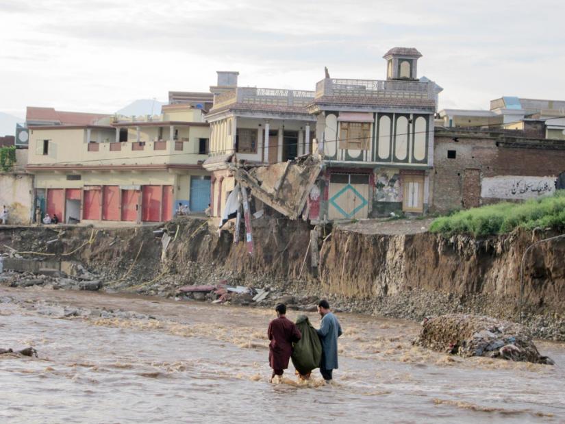 Two young men help an elderly woman along a flooded path in the Swat region of Pakistan
