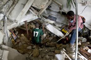 Two young men use crow bars and bare hands to dig through rubble in search of earthquake survivors