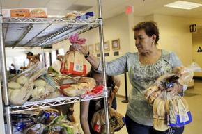 A woman sorts through a rack of breads and buns at a food pantry in San Jose, Calif.