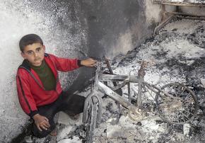 A boy in Daraa sits in the rubble of his damaged home
