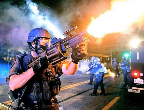 An officer in riot gear fires tear gas at protesters in Ferguson