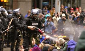Peaceful protesters sit in as riot police fire pepper spray during the 1999 WTO protests