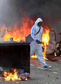 A man crosses through burning wreckage during rioting in London