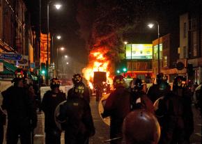 Riot police stand watch over a burning double decker bus