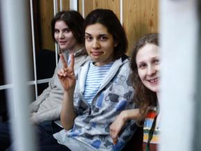 Members of Pussy Riot sit in the cage where they were confined during their trial