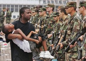 A Katrina survivor holds his young son in front of a line of soldiers