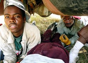 Haitian sugar cane workers in Dominican Republic take a 10-minute break under a truck, the only source of shade